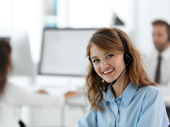 Junge Frau mit Headset sitzt lächelnd in einem Büro