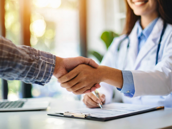 Eine Ärztin und ein Patient schütteln Hände. Es sind nur die  Arme und der Unterkörper der Ärztin zu sehen.